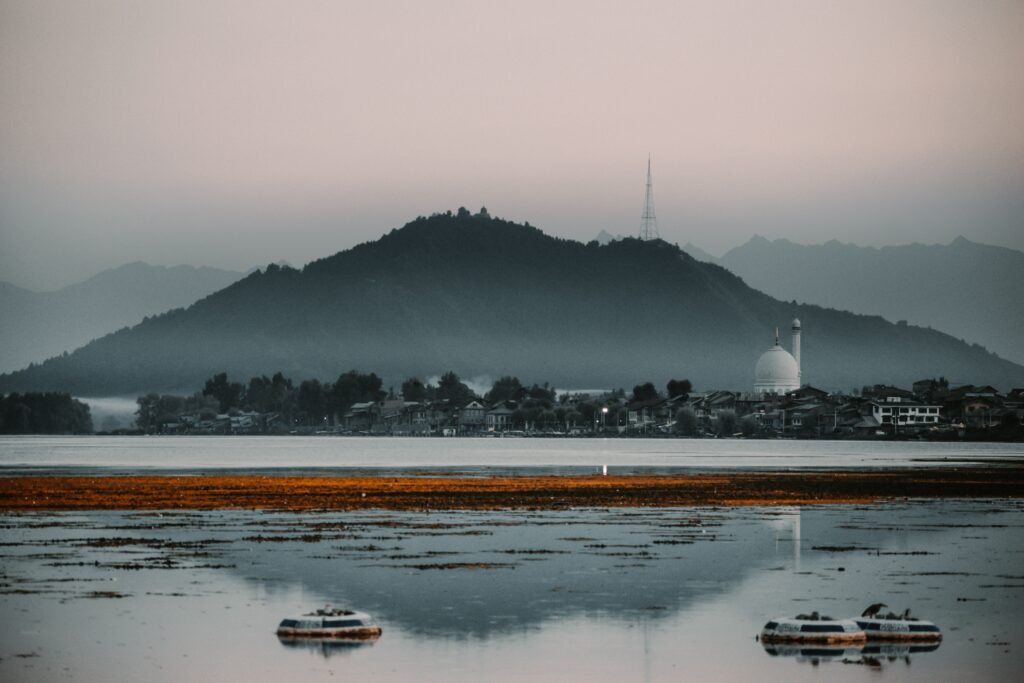 A tranquil view of Dal Lake with Hazratbal Shrine silhouetted against misty mountains in Srinagar, India.