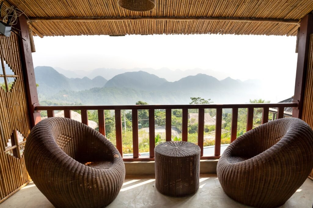 Comfortable armchairs and small side table on veranda near wooden barrier overlooking mountain ridge and green trees in tropical country