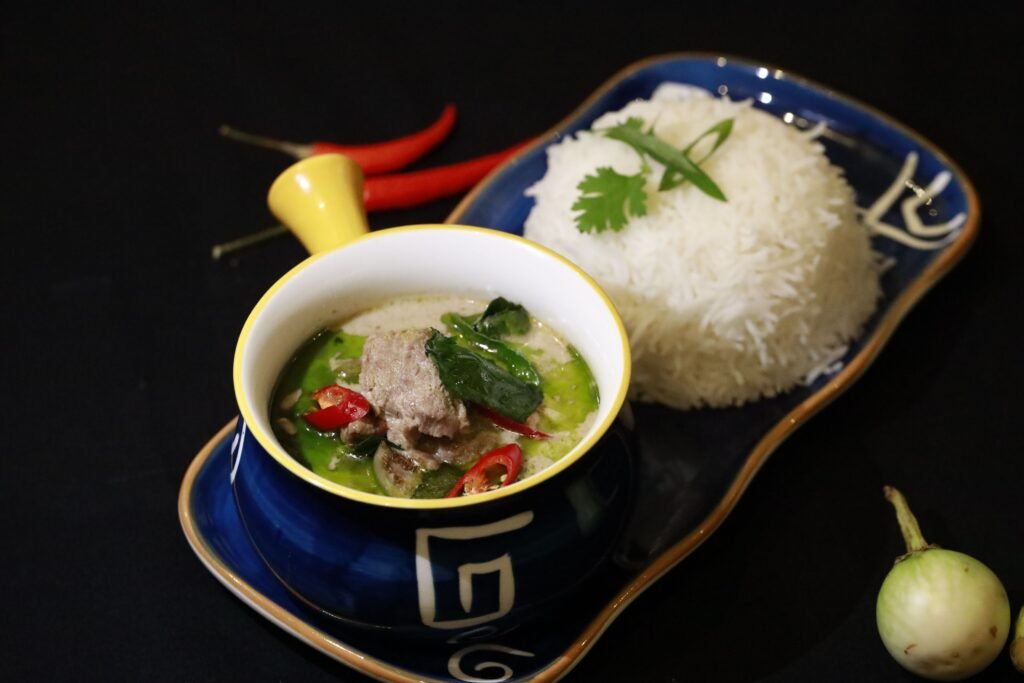 Close-up of Thai green curry with rice on a ceramic tray, garnished with chili.