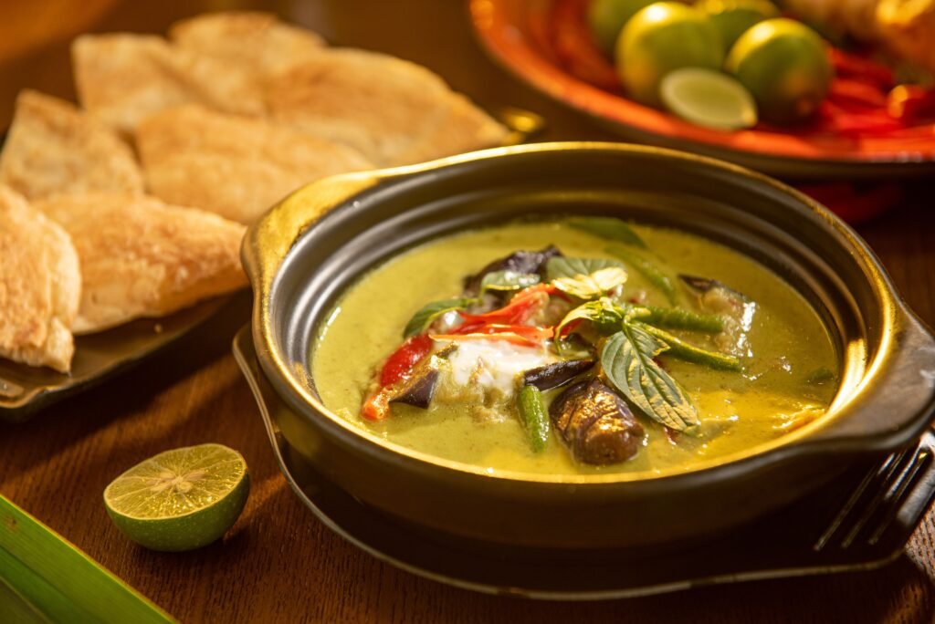 A flavorful Thai green curry with vegetables and aromatic herbs in a stylish black bowl.