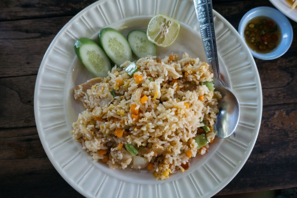 A plate of Thai fried rice with vegetables, served with cucumber and lime.