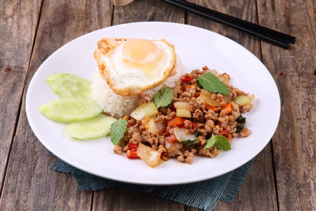 Thai stir-fry dish with rice and egg on rustic table setting, vibrant and appetizing.