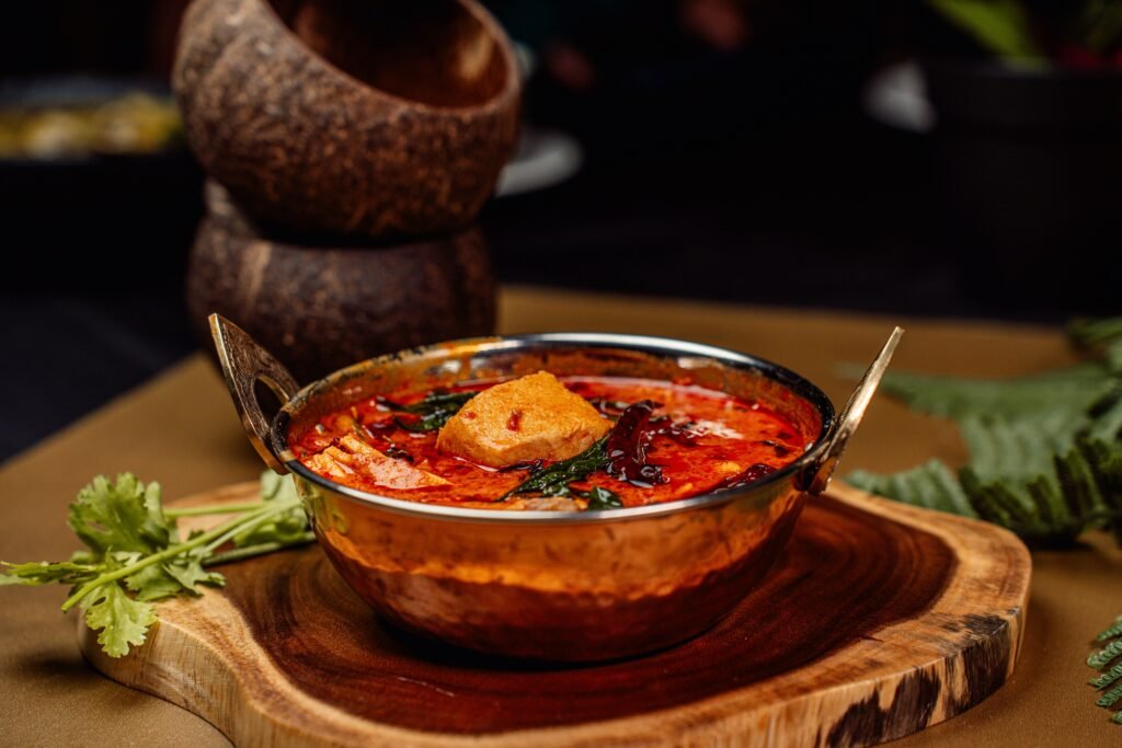 A vibrant Indian curry dish served in a traditional copper bowl on a rustic wooden platter.