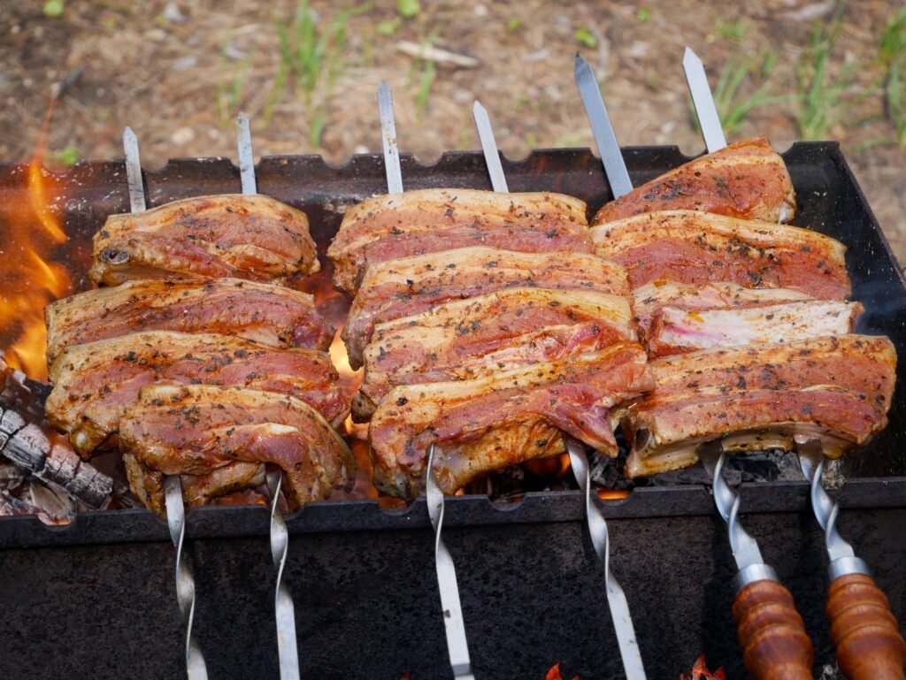 Juicy seasoned pork ribs grilling over an open flame on skewers outdoors, capturing the essence of a summer barbecue.